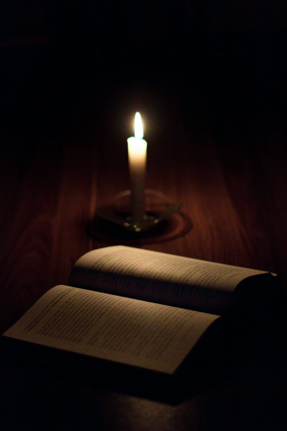 Ein aufgeschlagenes Buch, beleuchtet von einer einzelnen brennenden Kerze.